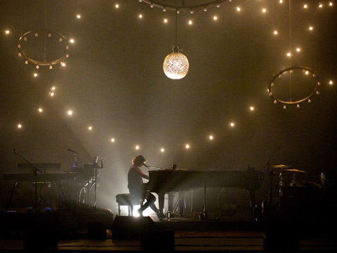 Sarah McLachlan playing piano on stage under strings of lights